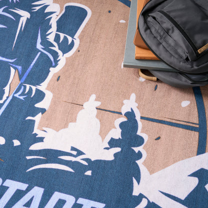 Blue and tan patterned rug with white mountain-like motifs; gray backpack atop stacked books.
