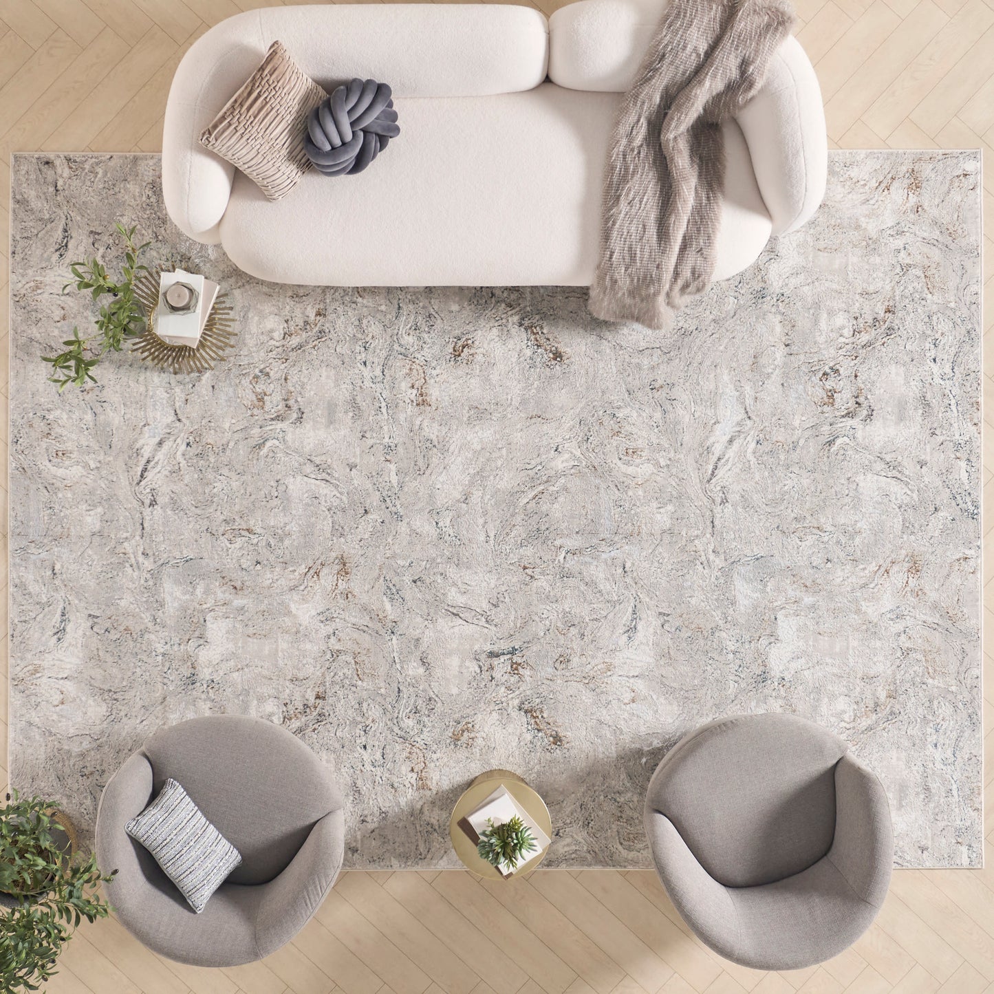 Overhead view of a neutral living room with a large marbled gray rug, cream sofa with knit throw, and two round gray chairs.