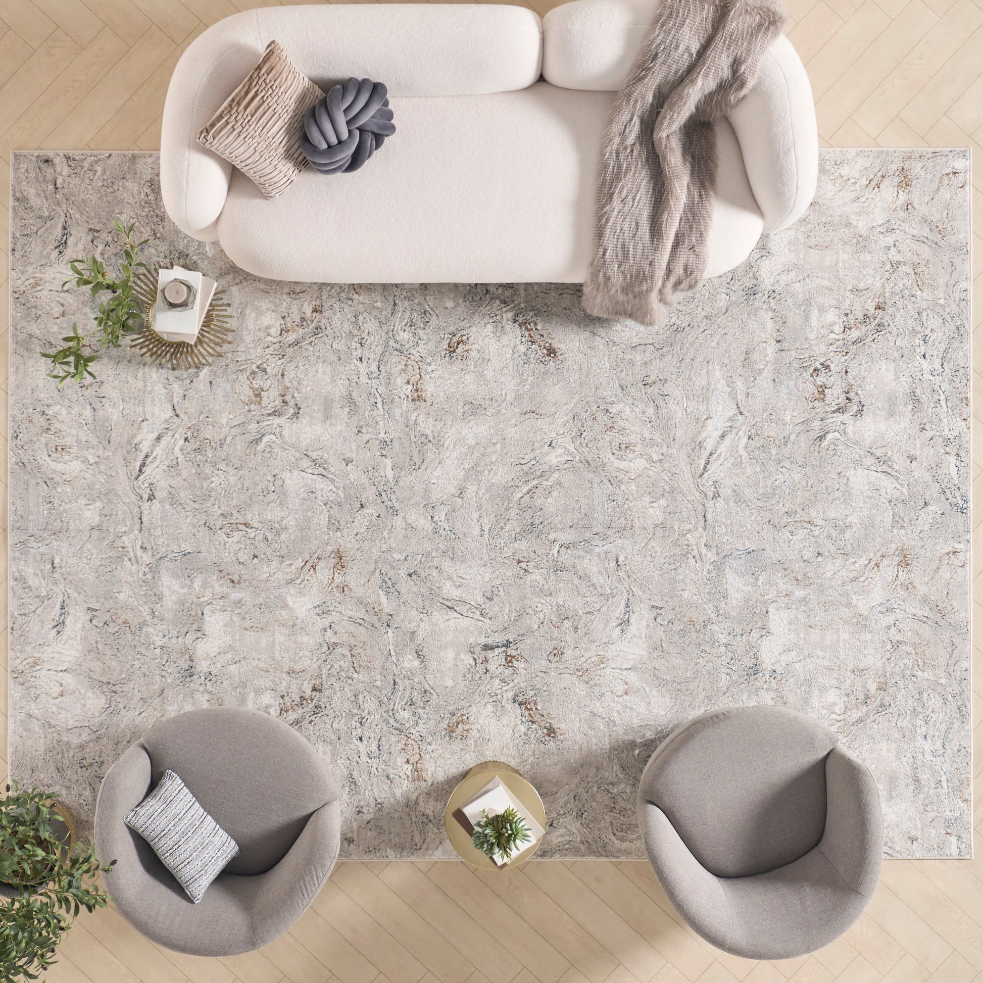 Overhead view of a neutral living room with a large marbled gray rug, cream sofa with knit throw, and two round gray chairs.