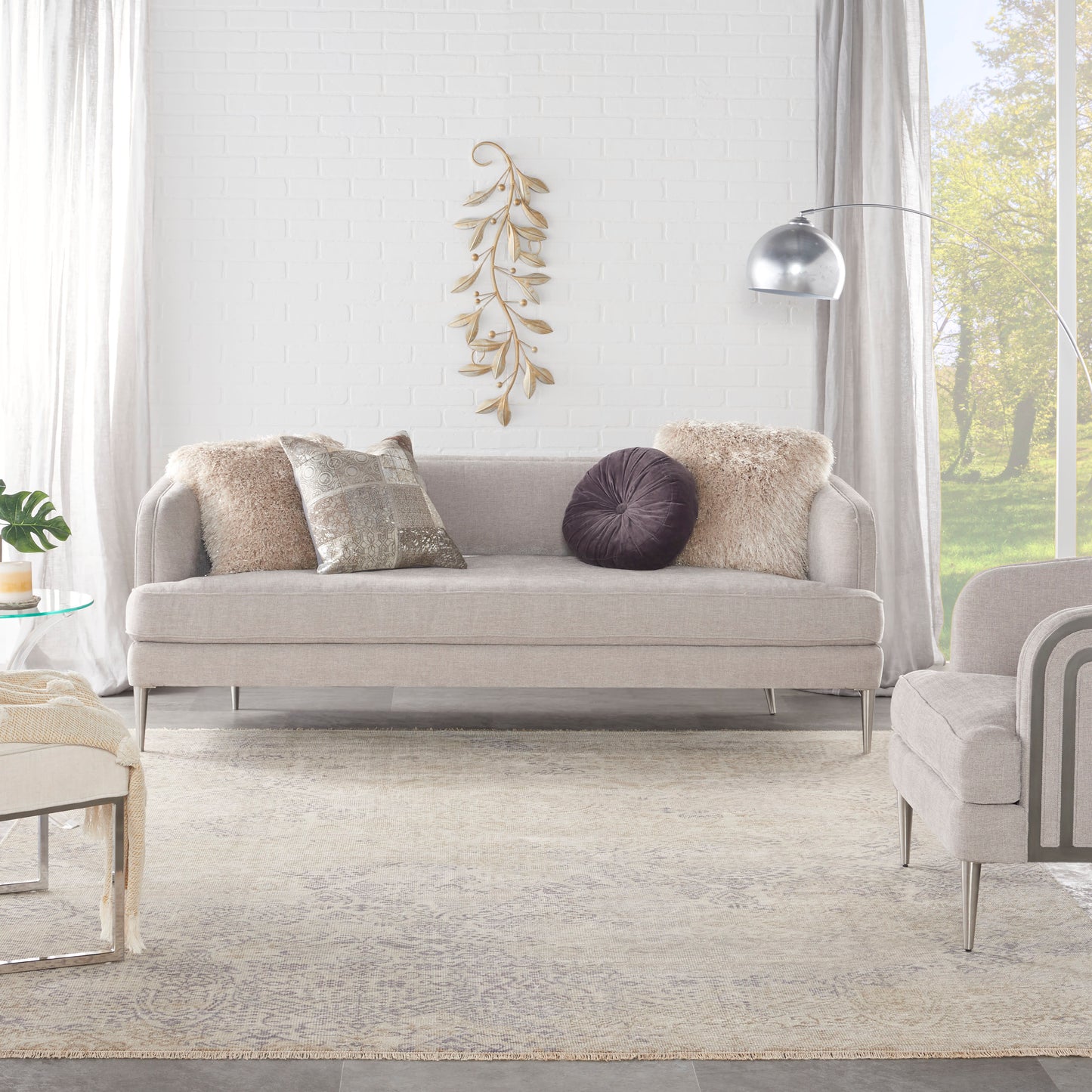 Vintage 8' x 10' rug in light gray on the floor of a modern living room, with an arc floor lamp, white brick wall, and dried leaf art.