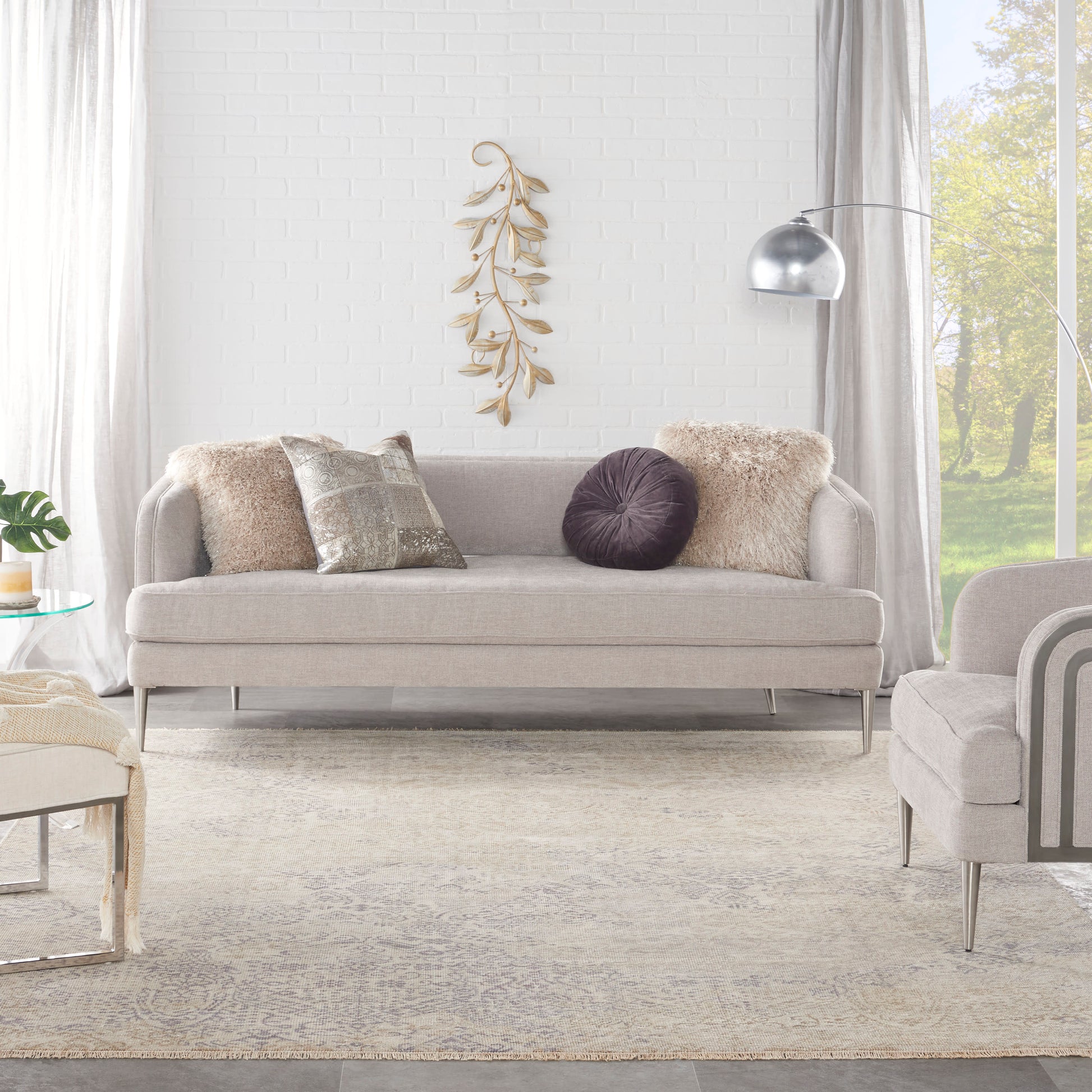 Vintage 8' x 10' rug in light gray on the floor of a modern living room, with an arc floor lamp, white brick wall, and dried leaf art.
