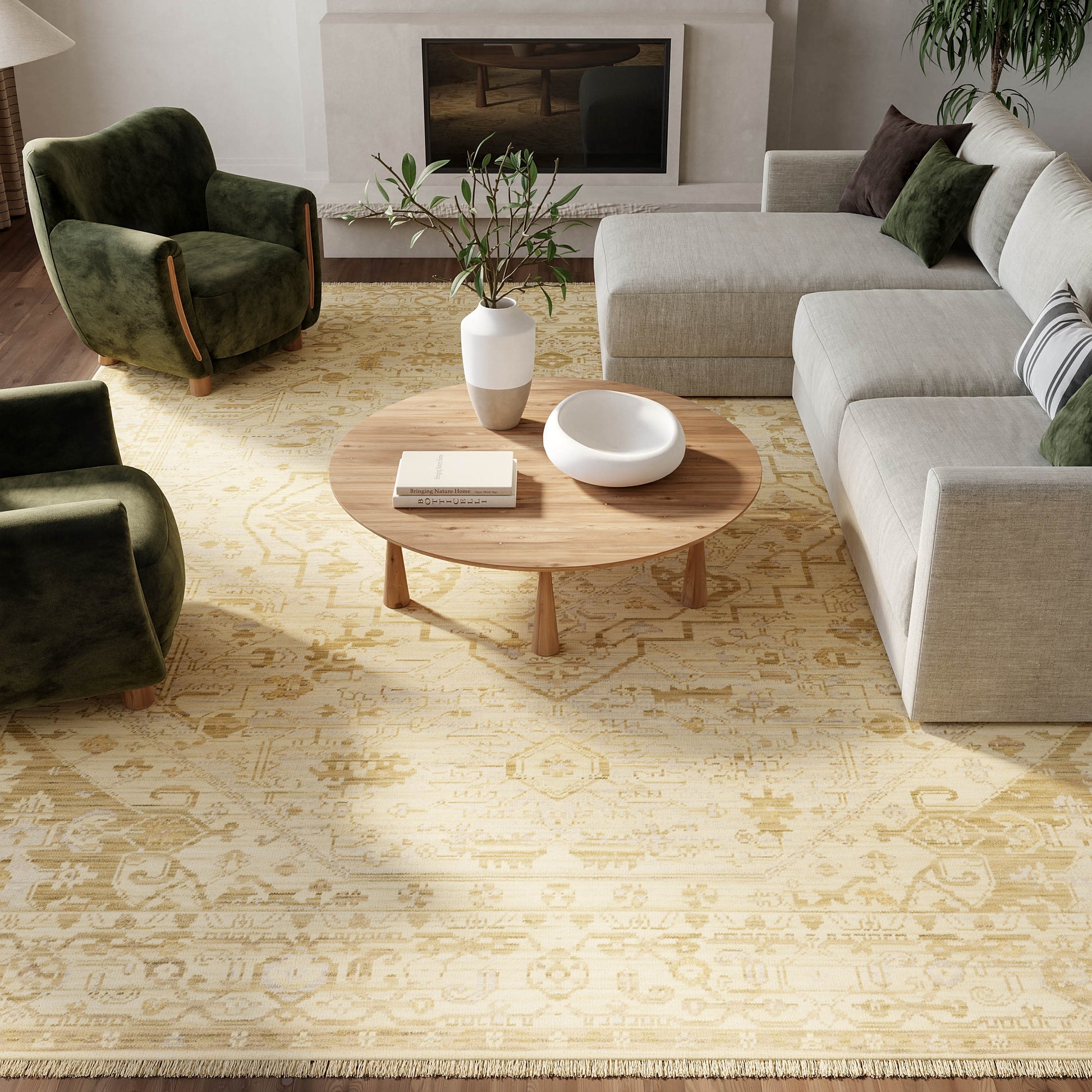 Cozy living room with beige rug, round coffee table, white bowl, vase of greenery, gray sectional and green velvet chairs.
