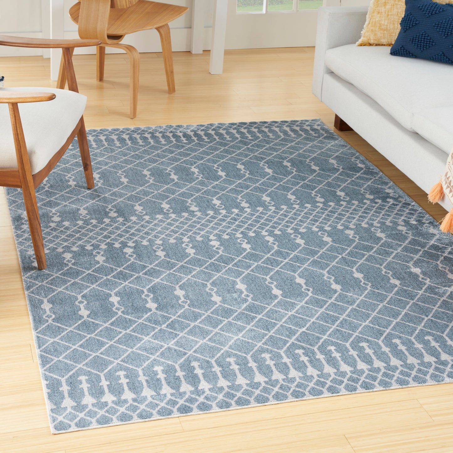 Blue-gray geometric lattice area rug on light wood floor in a living room with white sofa and mid-century chairs.