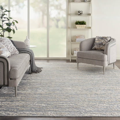 Blue-gray patterned rug in a bright living room, with a light gray fabric sofa & matching armchair on metal legs, and white shelving.