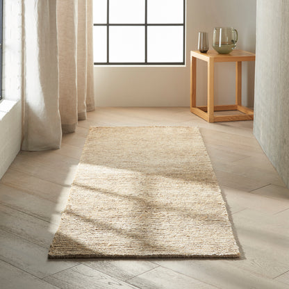 Beige jute runner rug on light wood floor in a room, with sheer curtains and a small wooden side table holding glassware.