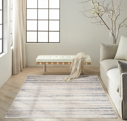 Neutral living room with gradient blue-gray rug, white tufted bench with wood slats & chrome legs, beige throw, gray sofa.