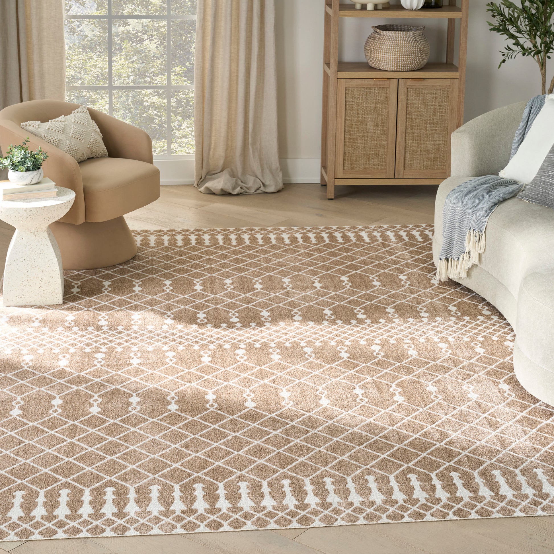 Cozy living room featuring a tan lattice rug, curved beige chair, light sofa with throw, woven cabinet and greenery