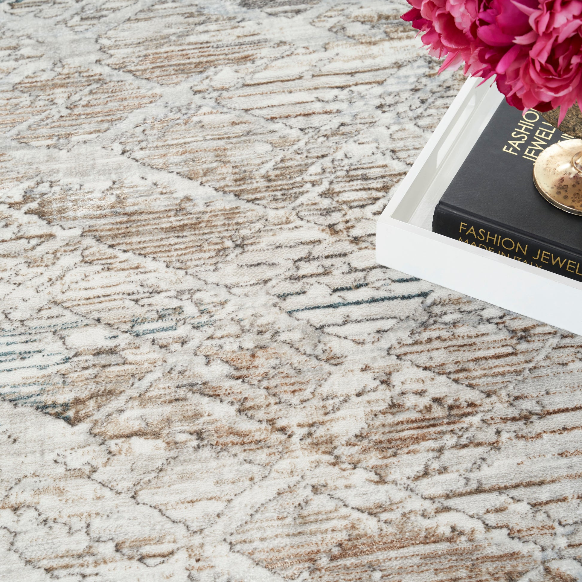 Cream patterned area rug with brown swirls; white tray with a black fashion jewelry box, a gold pendant, and pink peonies.