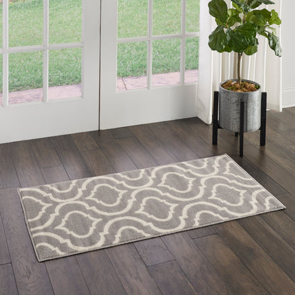 Grey rectangular rug with white wavy geometric pattern on dark wood floor beside glass doors, potted plant nearby.