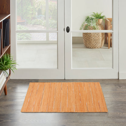 Rectangular orange flat-weave rug in front of glass-paned white doors & dark wood floor; nearby houseplants.