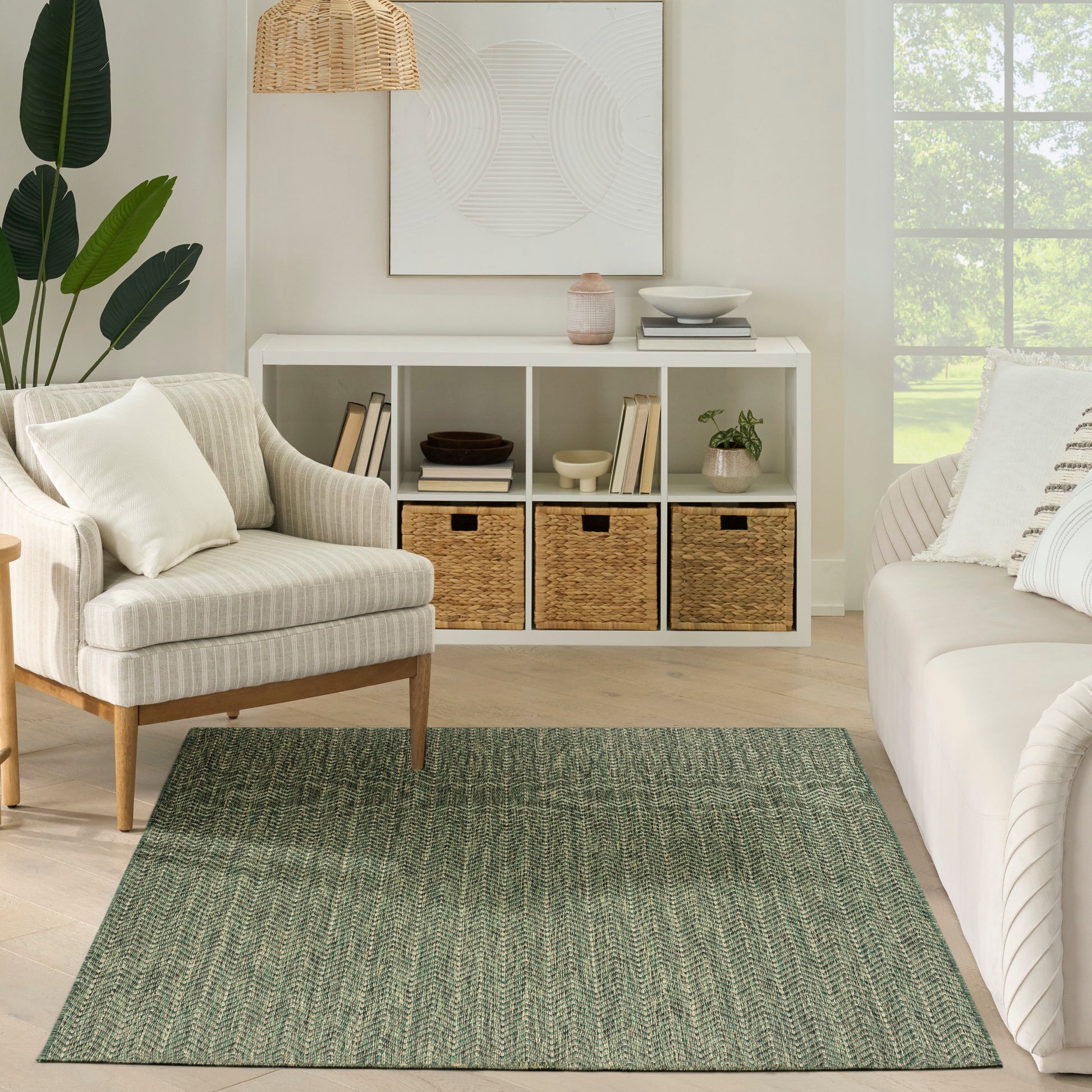 Neutral living room with sage green woven rug, beige striped armchair, white cubby shelf with wicker baskets, plants.
