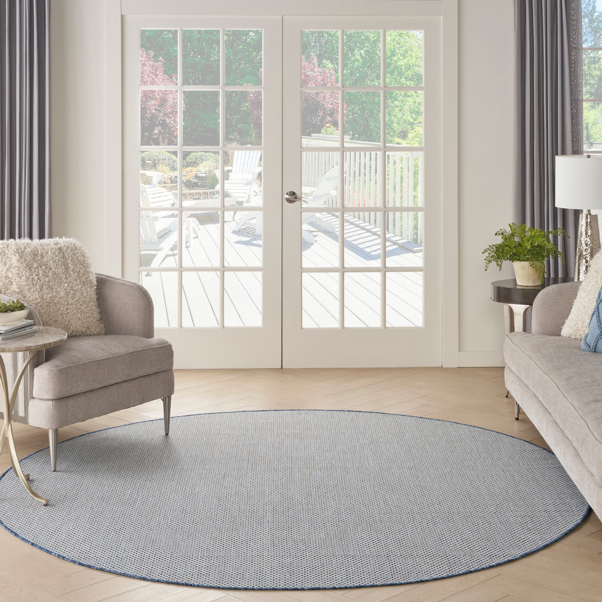 Bright living room with French doors, round blue-gray rug, beige sofa & armchairs, plant and side table