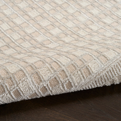 Beige geometric patterned area rug with cream and tan squares, thick tufted pile, bound edge on dark wood floor.