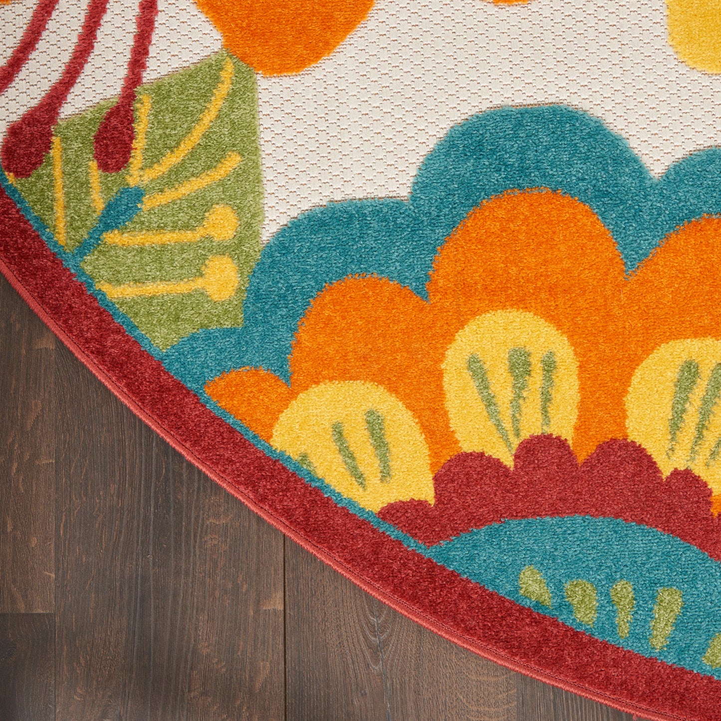 Colorful circular floral rug corner with red border on dark wood floor; bright teal, orange, yellow, and green petals.