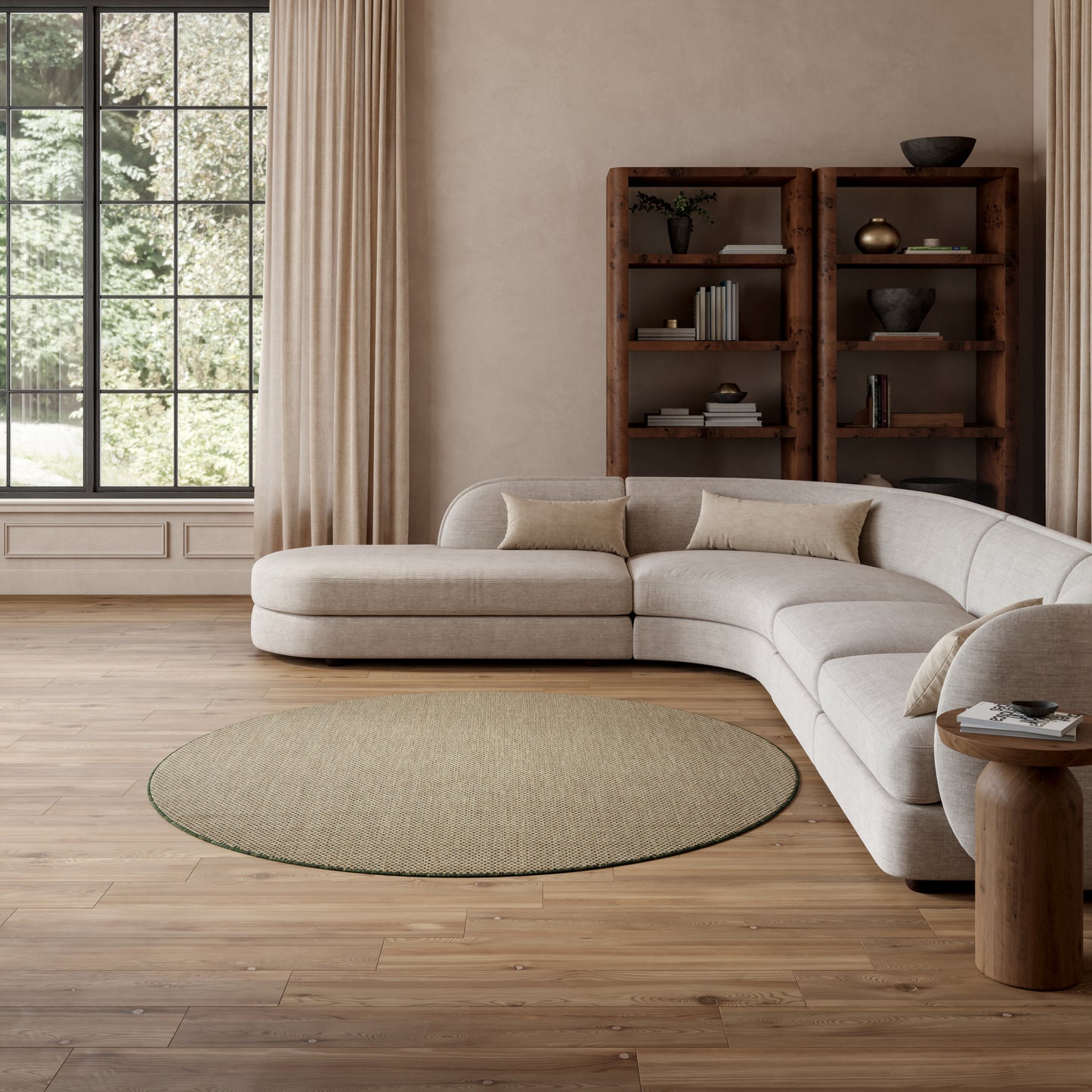 Beige L-shaped sectional sofa in a bright living room with a round natural fiber rug, wood bookshelf, and tall windows.