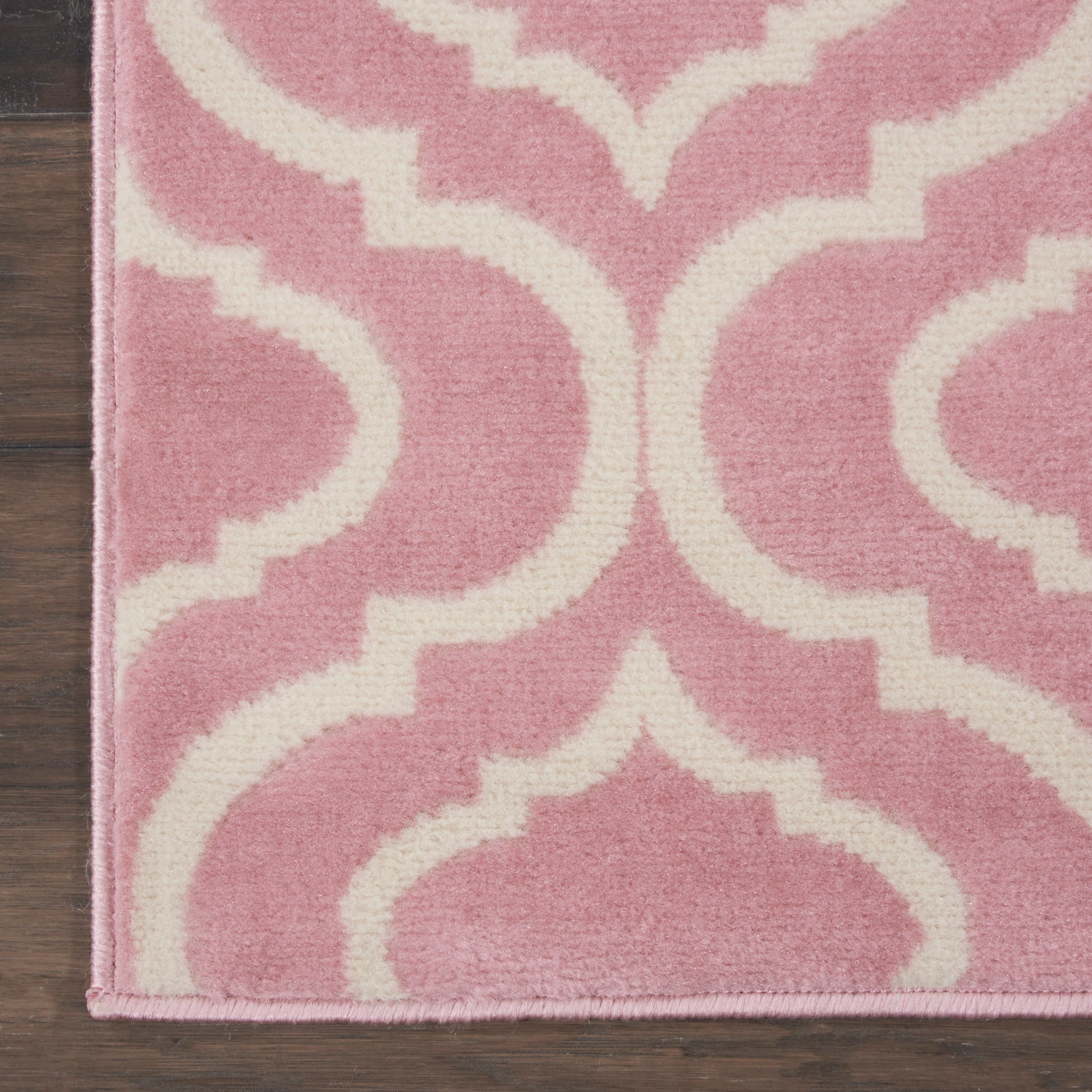 Pink and white trellis-pattern rug with plush texture on dark wood floor.