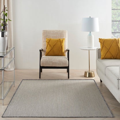 Cozy living room with beige patterned armchair, dark legs, mustard cushions, round side table, blue lamp, and grey rug.