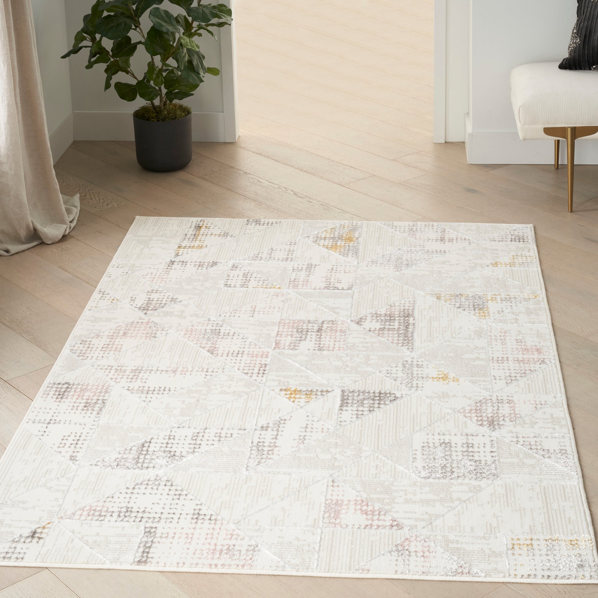 Neutral geometric rug with patchwork triangles in beige, gray and pale pink on a light wood floor in a modern living room.