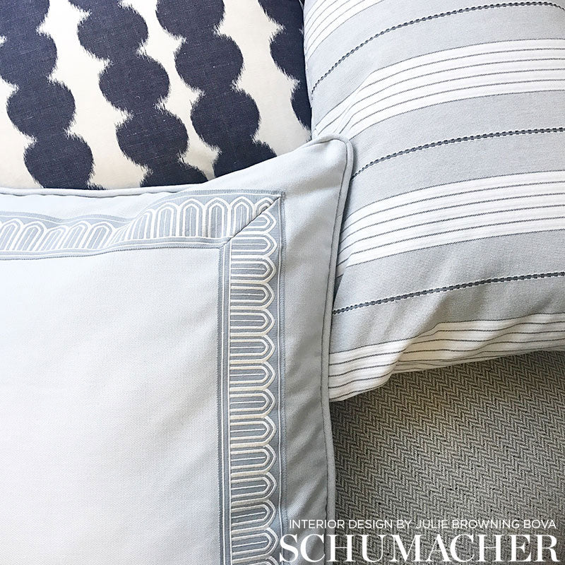 Blue-gray decorative pillows with embroidered border, striped pale-blue pillow, navy ikat cushion on grey herringbone sofa.