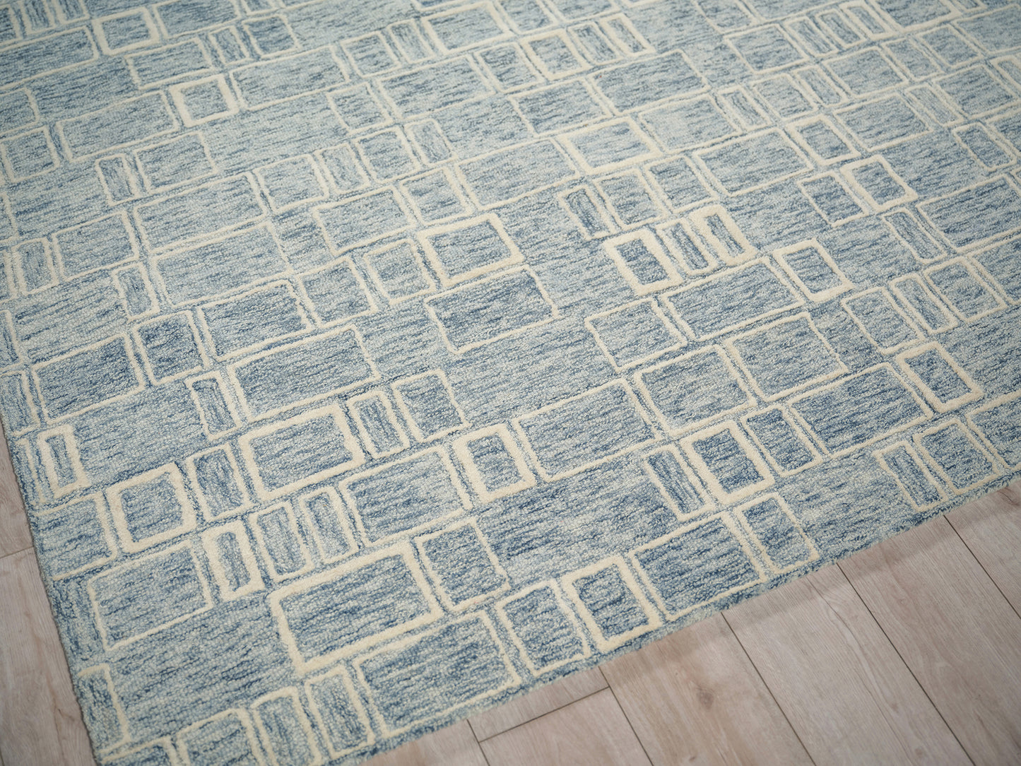 Blue geometric rug with cream rectangular grid pattern on light wood floor; modern, low-pile weave.
