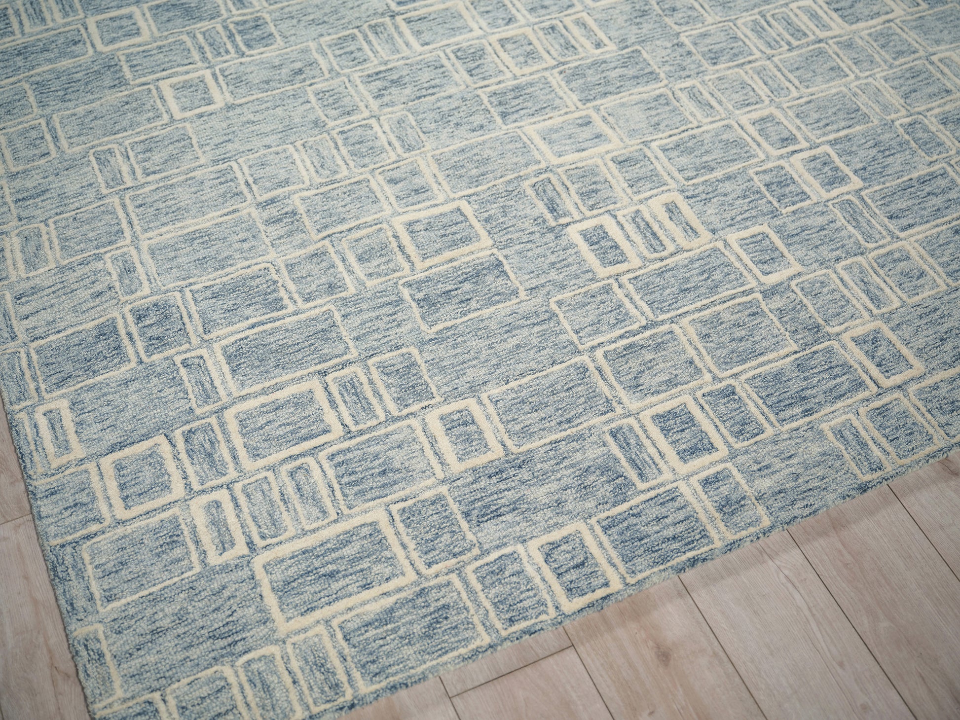 Blue geometric rug with cream rectangular grid pattern on light wood floor; modern, low-pile weave.