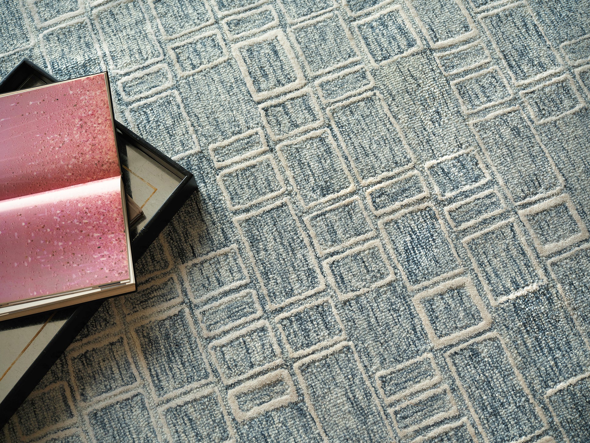 Blue geometric area rug with interlocking square pattern; pink glitter gift boxes in the corner.