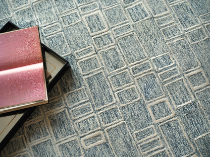 Blue geometric area rug with interlocking square pattern; pink glitter gift boxes in the corner.