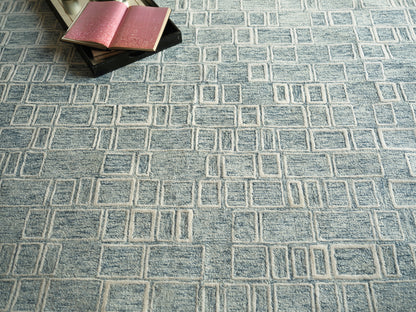 Blue rug with square-grid geometric pattern; top-left corner shows small black books with pink pages.