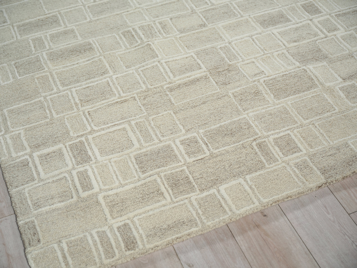 Beige area rug with a light rectangular grid pattern laid on a pale wood floor.