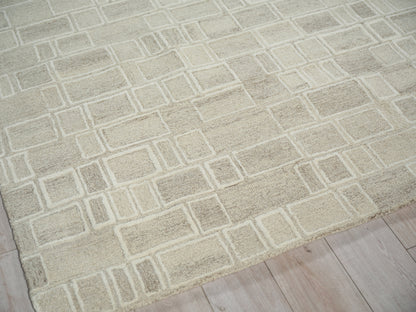 Beige area rug with a light rectangular grid pattern laid on a pale wood floor.