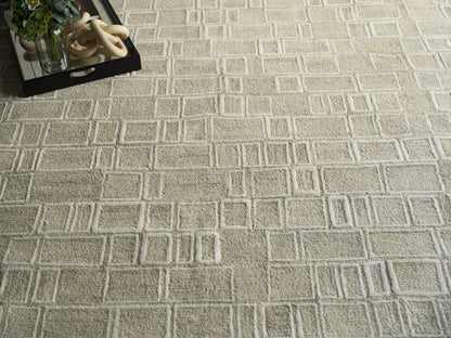 Beige geometric area rug with a raised square grid; top-left shows a black tray, plant, and beige ring sculpture.