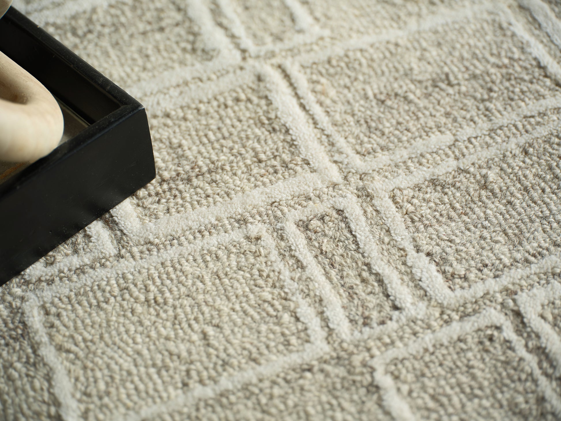 Beige textured geometric rug with a black rectangular box on it and a partial bare foot visible inside the box.