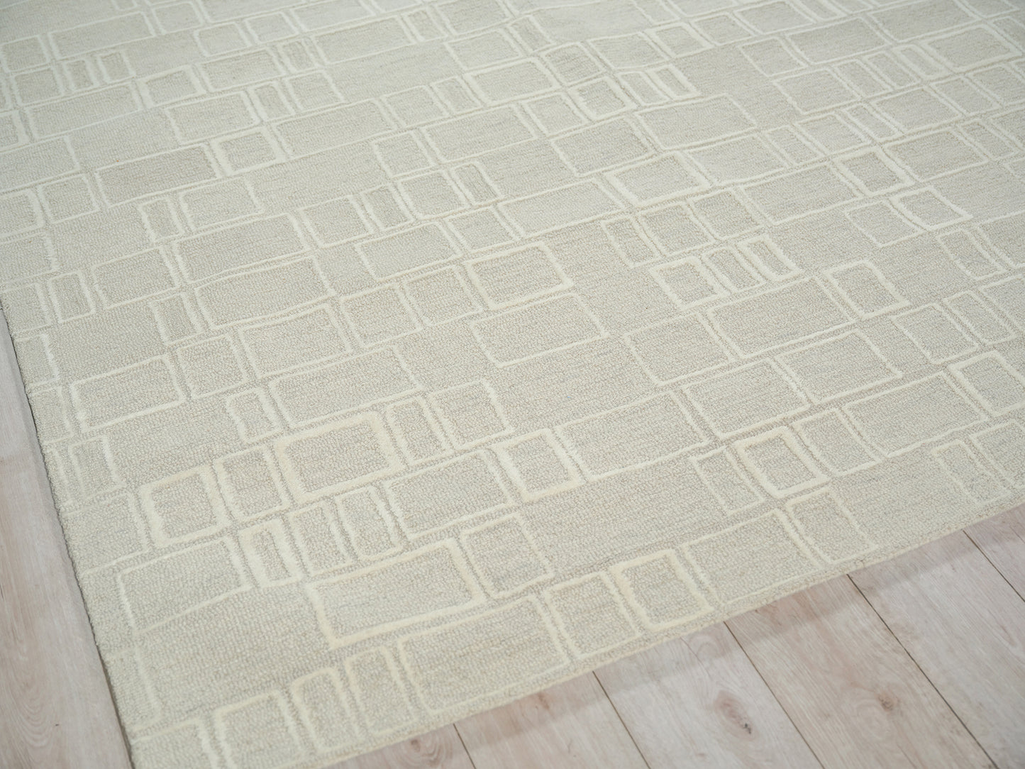 Cream textured rug with geometric outlined rectangles on light wood floor.
