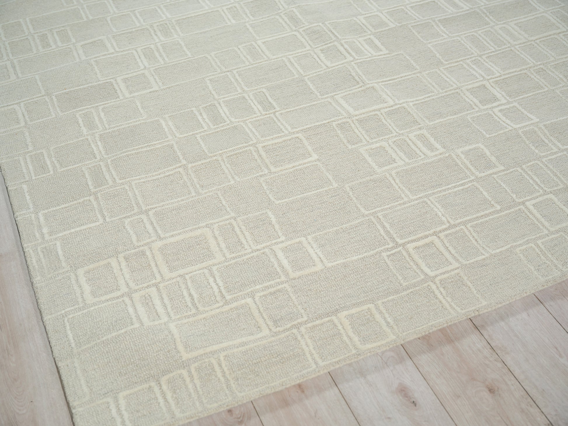 Cream textured rug with geometric outlined rectangles on light wood floor.