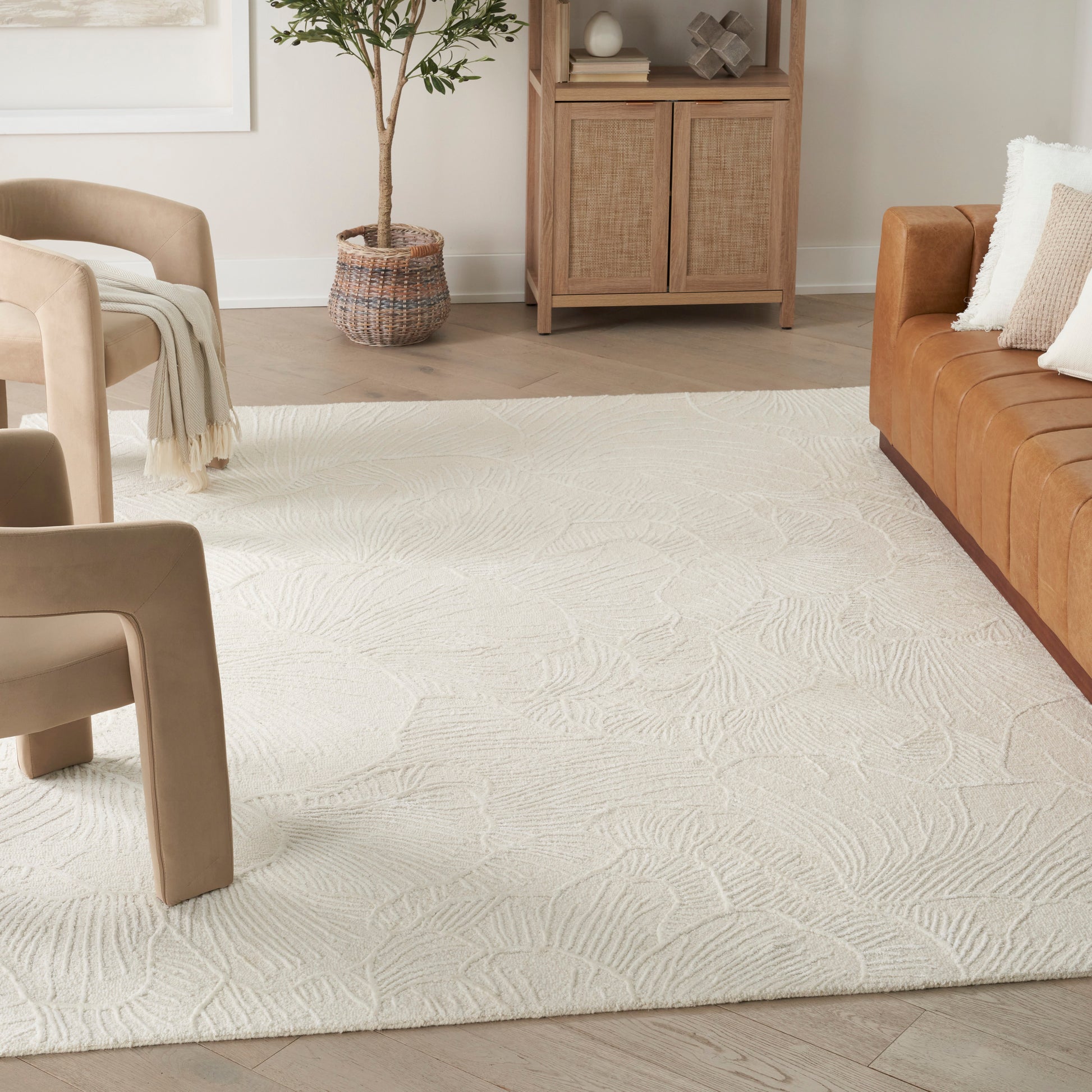 Cream textured area rug with a palm-leaf pattern in a cozy living room with tan leather sofa and beige chairs.