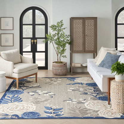 Living room with arched black doors, beige sofa with blue cushions, white armchair, woven cabinet, blue floral area rug.