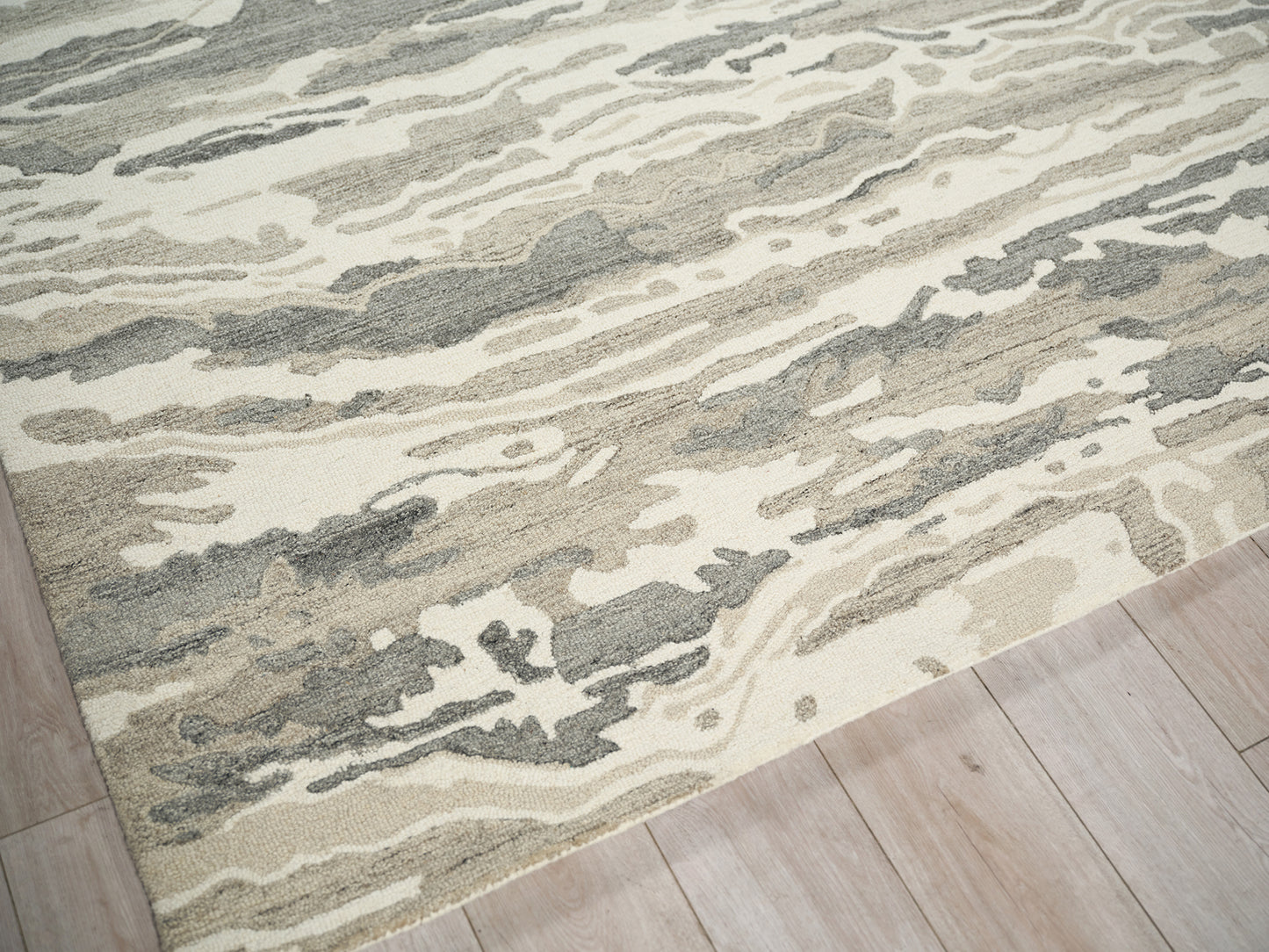 Abstract beige, gray and cream area rug with marbled pattern on light wood floor.
