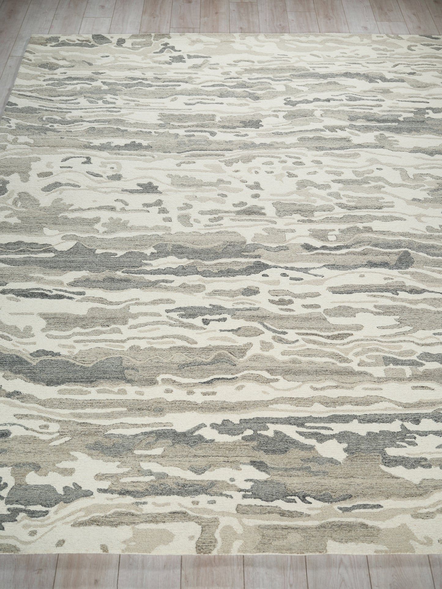 Abstract beige and gray rug with cream and taupe wave pattern on light wood floor.