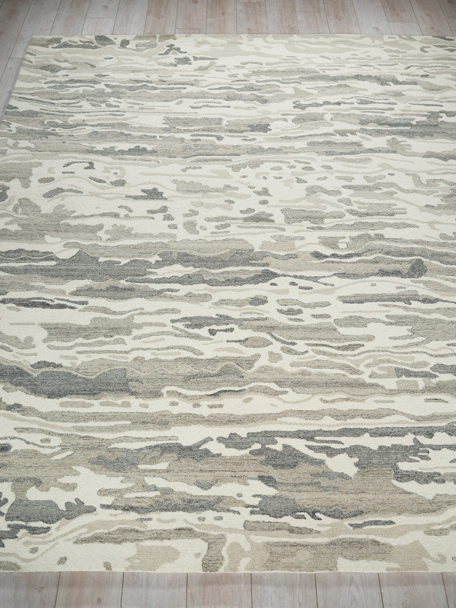 Abstract beige and gray rug with cream and taupe wave pattern on light wood floor.