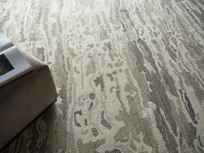 Abstract gray and beige rug with a wavy pattern beside a light tan ottoman and an open magazine.