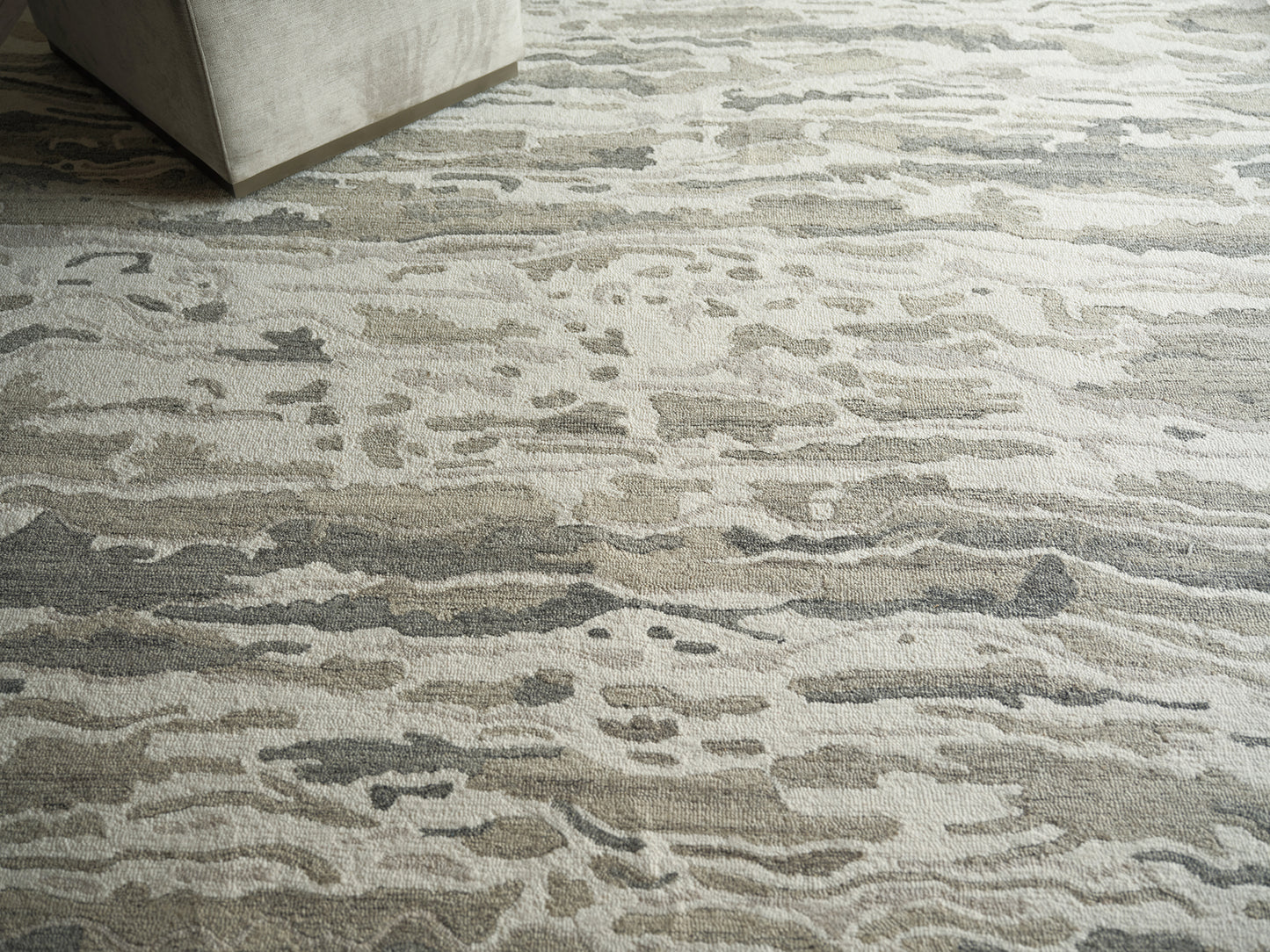Neutral abstract area rug in beige, gray and taupe with organic wave pattern under a light gray sofa.