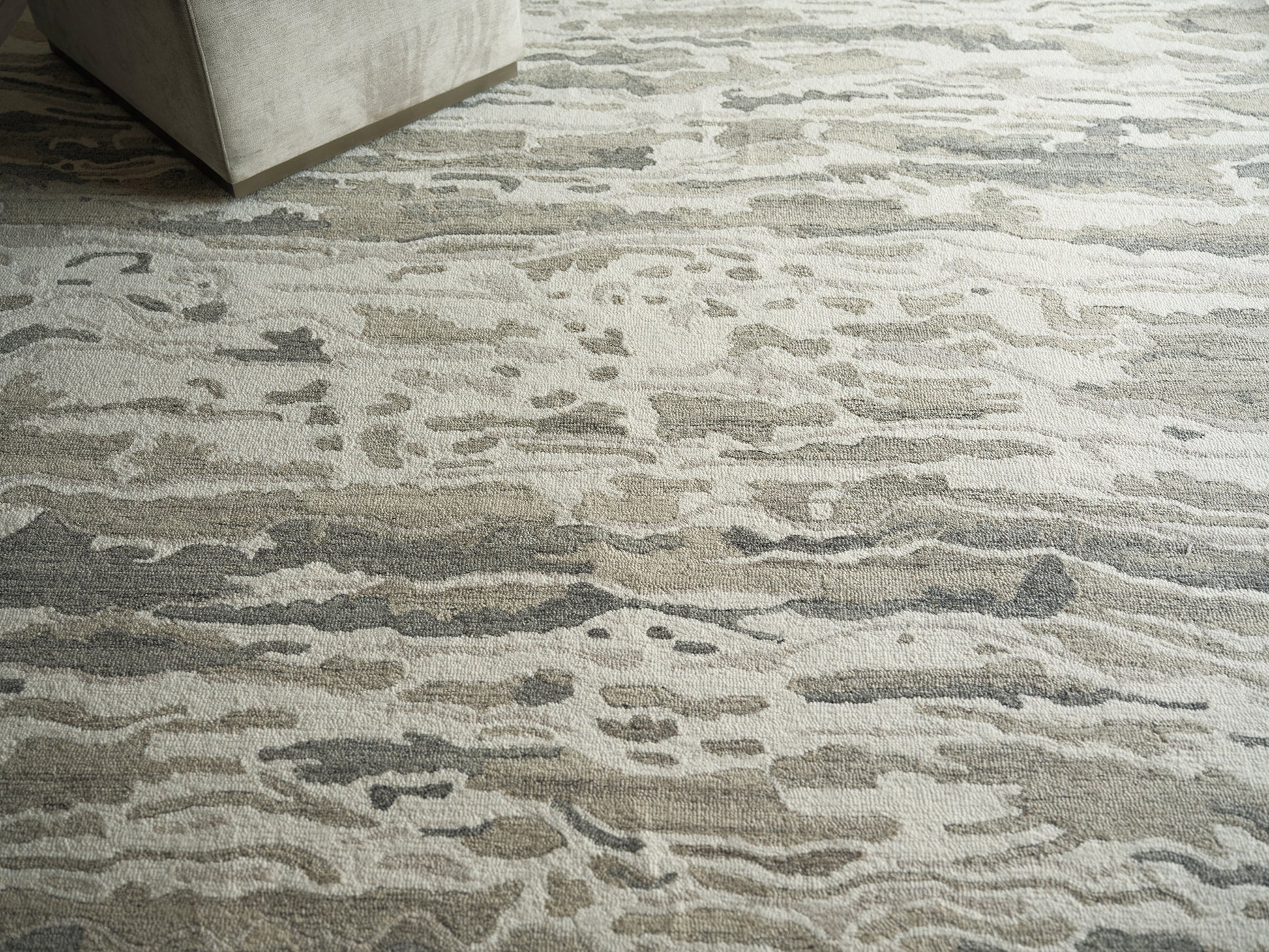 Neutral abstract area rug in beige, gray and taupe with organic wave pattern under a light gray sofa.