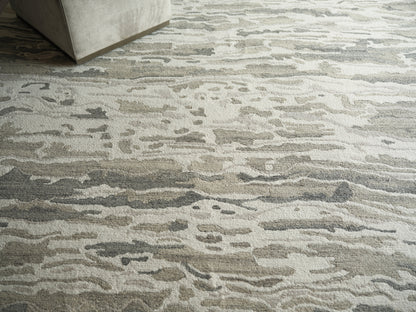 Neutral abstract area rug in beige, gray and taupe with organic wave pattern under a light gray sofa.