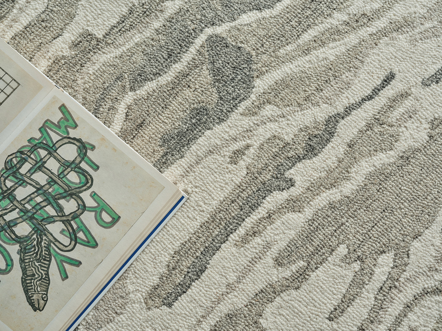 Beige-gray textured rug with a wavy abstract pattern; open art book with green doodles resting on it