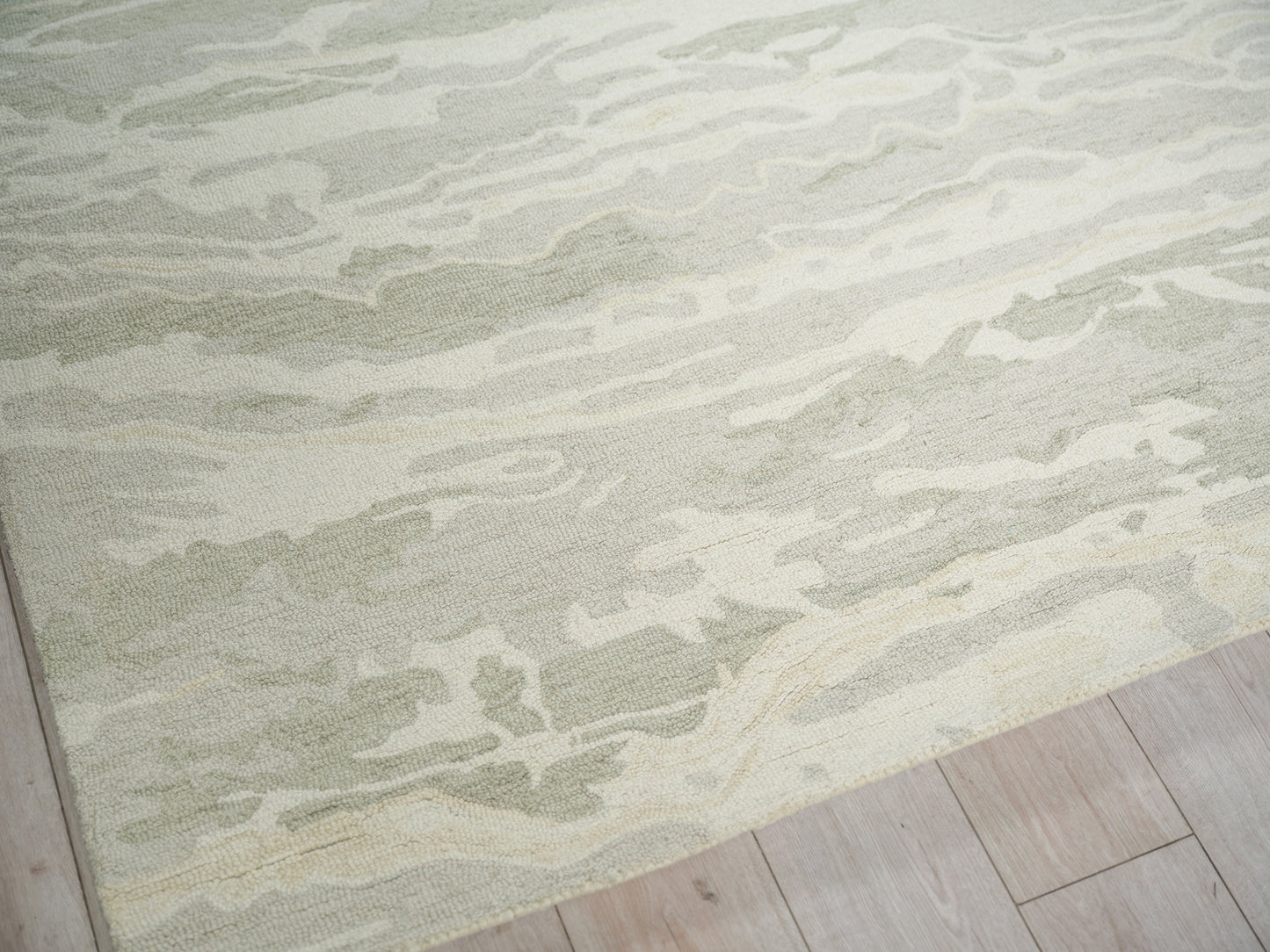 Soft green and cream abstract patterned area rug with plush pile on light wood flooring.