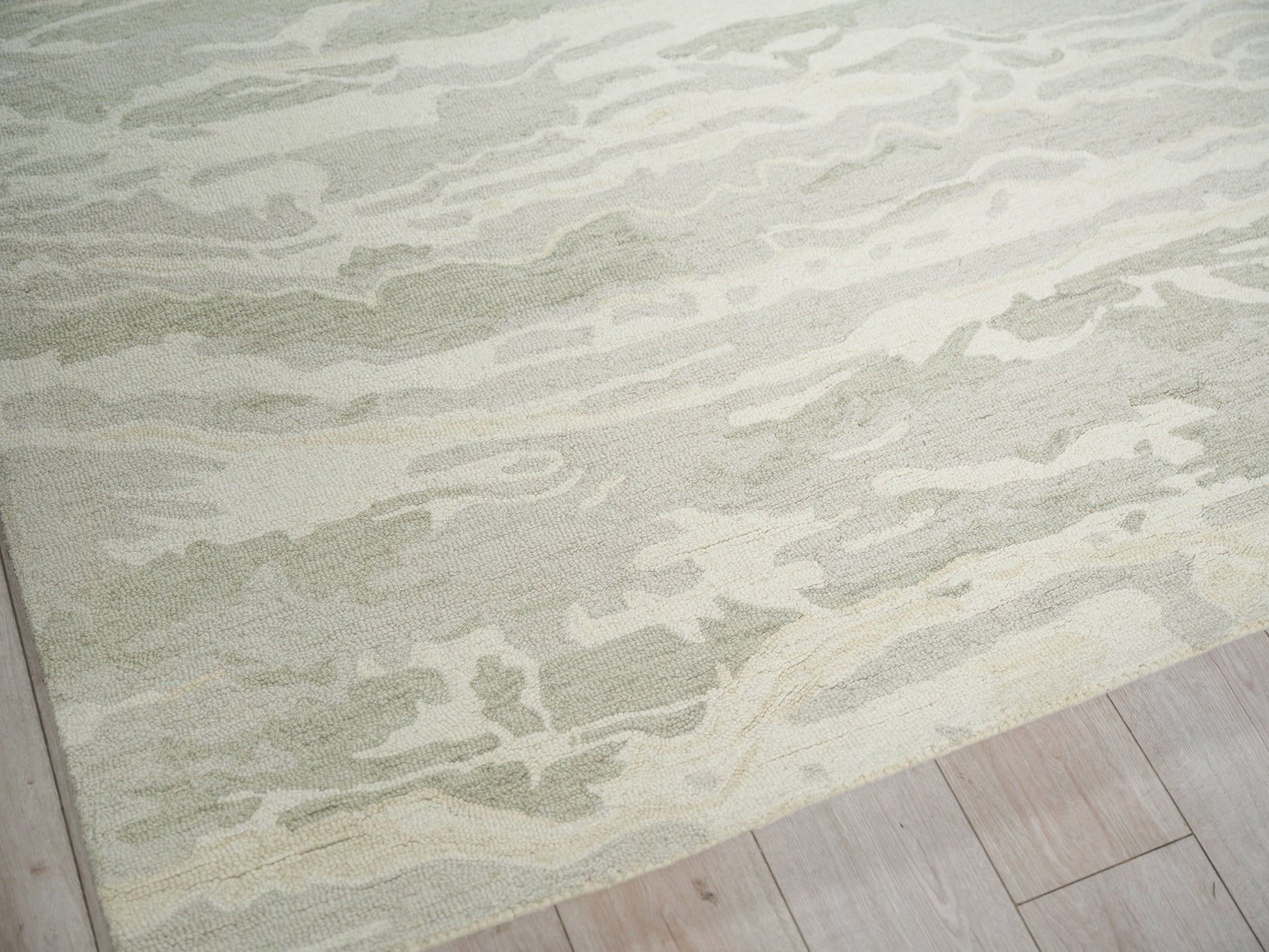 Soft green and cream abstract patterned area rug with plush pile on light wood flooring.