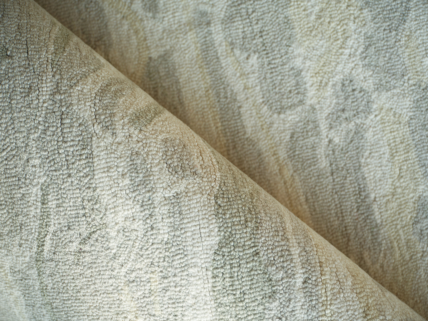 Close-up of soft beige-gray boucle-textured rug fabric, folded for cozy rug use.