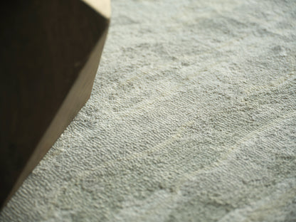 Close-up of light gray textured loop-pile rug with a brown cardboard box at the left edge.