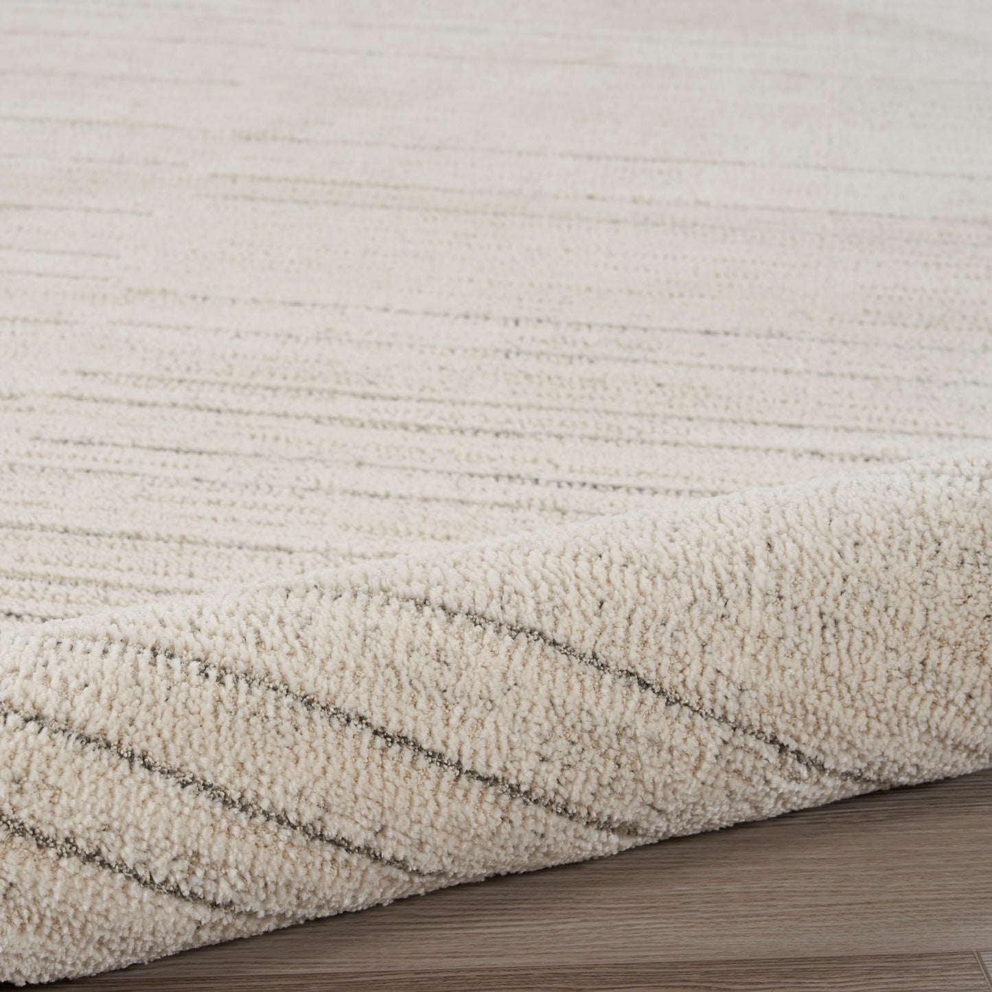 Beige textured rug with soft loop pile and diagonal stripes, resting on light wooden floor.