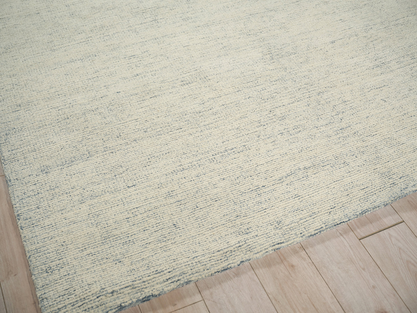 Rectangular hand-tufted rug in pale blue and cream on light wood floor, with a subtle striped texture.